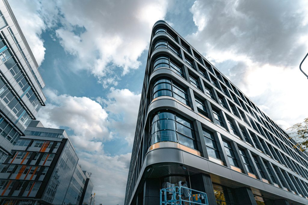 pexels-photo-16846525-16846525 Low angle view of a modern office building with a sleek glass facade against a cloudy sky.